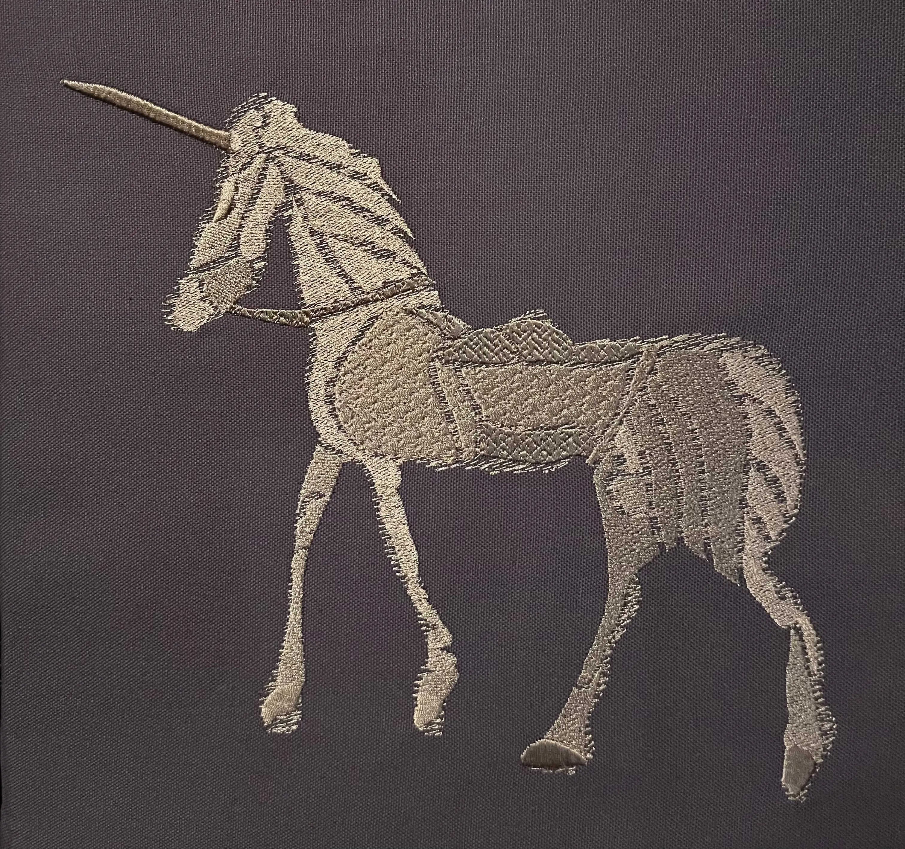 Gesticktes Einhorn in Gold auf grauviolettem Stoff