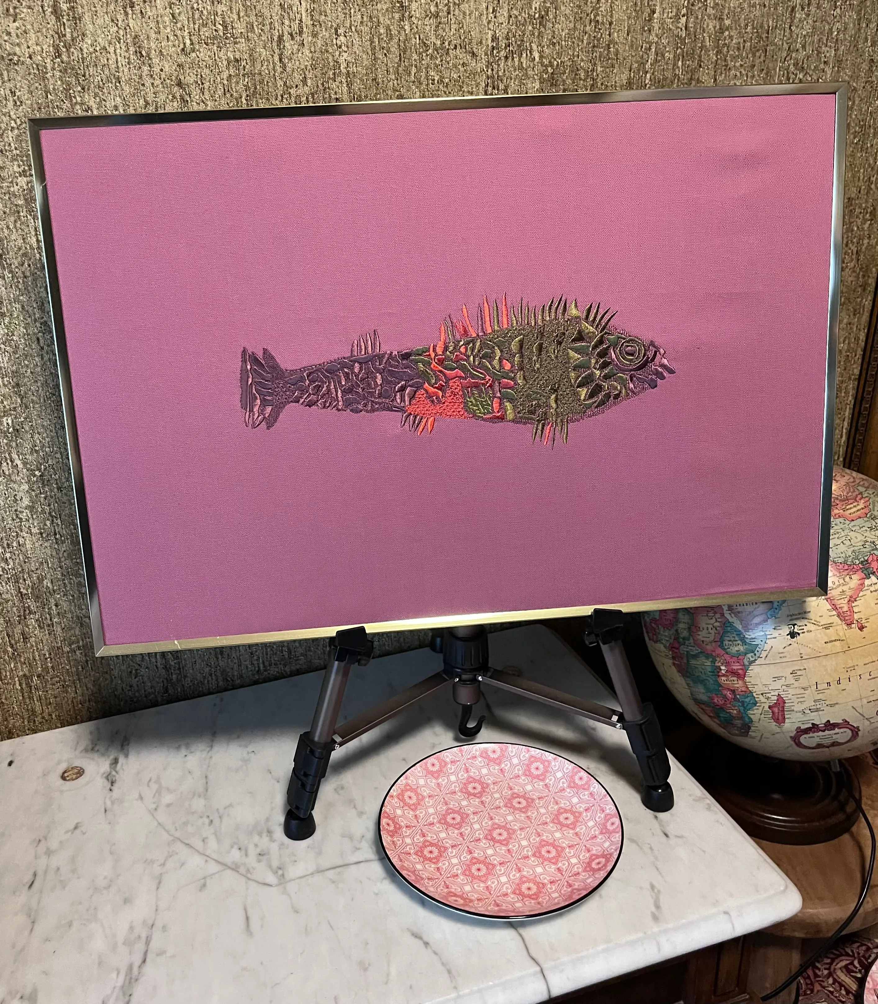 Gestickter Fisch auf rosa Stoff, gerahmt auf einer Staffelei