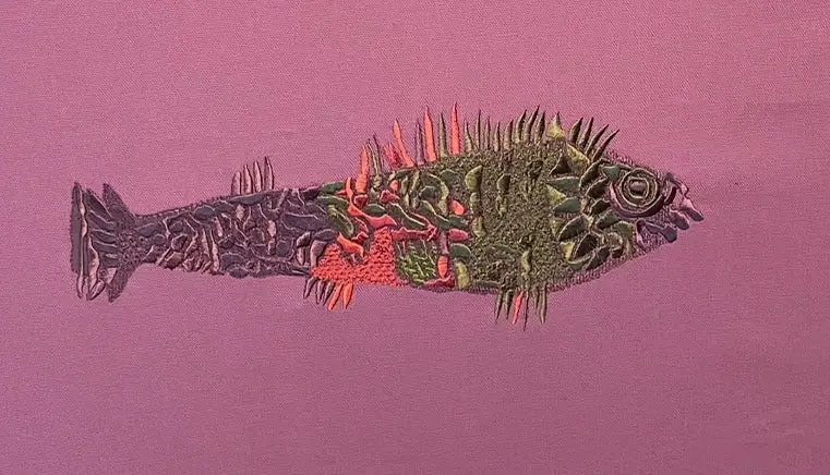 Detailansicht eines gestickten Fisches in Grün, Rot und Violett auf rosa Stoff