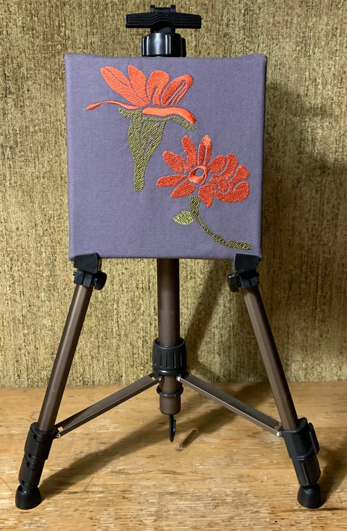 Orange Blüten mit grünem Stiel gestickt auf grauen Stoff