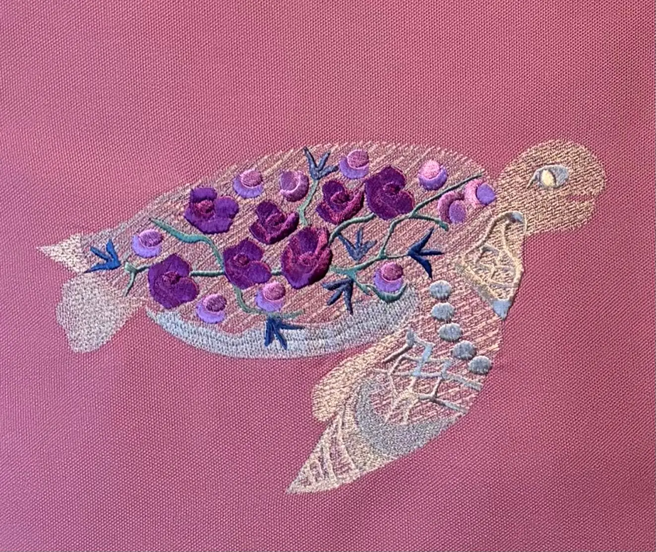 Gestickte Schildkröte mit violetten Rosen auf dem Panzer auf rosafarbenem Stoff